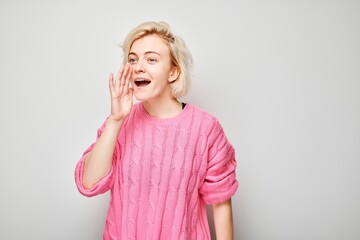 Portrait of blonde girl shouting loudly with hands, news, palms folded like megaphone isolated on...