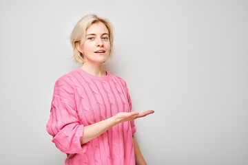 Young blond woman in pink sweater holding something in hand, demonstrating empty space for product...