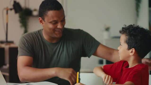 An African American father helps son with school homework, gives him high five