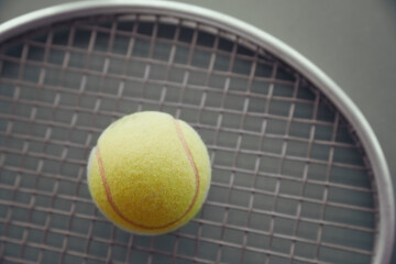 yellow tennis ball lies on a tennis racket on a gray background
