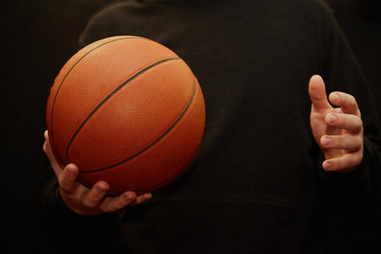 Basketball ball is being tossed from hand to hand on a dark background in warm orange light close-up, basketball ball in hands dark background