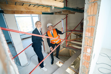 Cheerful businesswoman and construction foreman standing under scaffolding inside house