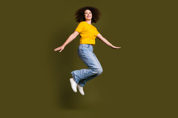 Fototapeta na wymiar Full length photo of young sportive woman with wavy hair jumping in casual garment have fun rejoice isolated on khaki color background