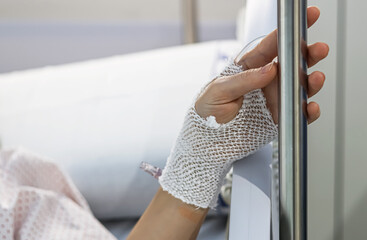 A woman's hand with a bandage and an intravenous line, in a hospital bed. Space for text