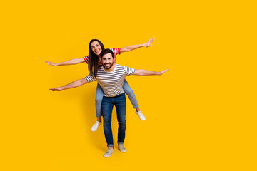 Fototapeta na wymiar Full length photo of carefree couple boyfriend holding on back pretty girl hold arms like wings isolated on vivid yellow color background