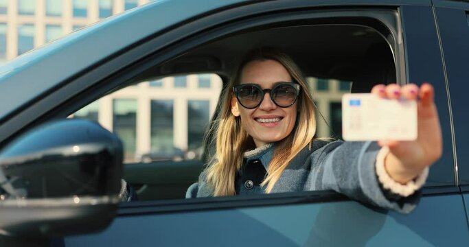 happy woman showing her new driver license out of car window