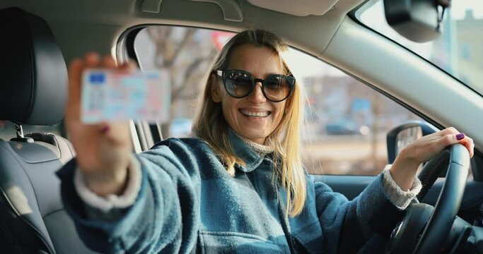 happy woman sitting in car and showing her new driver license