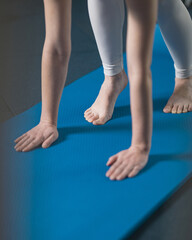Pilates exercise on carpet. Feet and hands of young woman in frame. Stretching training. Element of asana in yoga. Transition to handstand. Palms pressed to floor. Side view. Blue background.