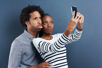 Love, funny face and couple with selfie in studio for silly, joke or bonding on grey background....