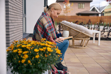 Woman sitting on doorstep when drinking coffee and reading book