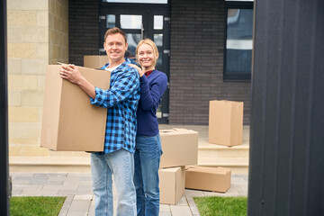 Cheerful man handling box and satisfied woman standing behind him