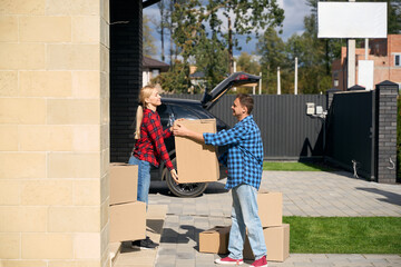 Amused man gives box to happy woman standing on doorstep