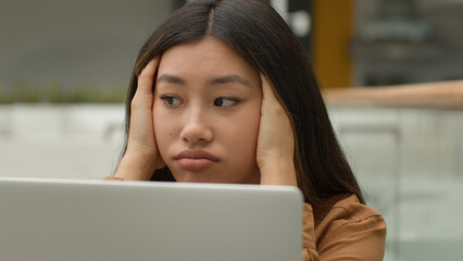 Exhausted overworked Asian woman girl student studying online work on laptop in office hold head headache tired chinese korean female employee businesswoman upset job failure despair fatigue burnout