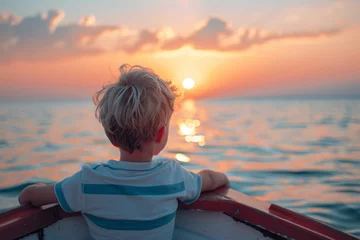 Poster Close-up of a boat, the boy has a white and blue T-shirt and blond hair. He is looking at the sea at sunset © Maelgoa