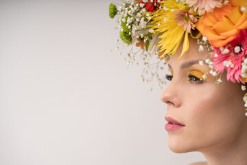 An intimate perspective of a woman adorned with a lush floral crown, her gaze directed slightly off-camera. The delicate interplay of shadow and light enhances the composition.