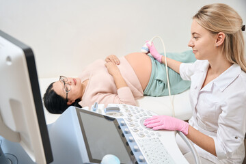 Smiling woman gynecologist making ultrasound of woman on second trimester