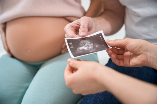 Close-up man holding the ultrasound picture of his baby in wife's womb