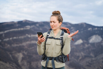 Young female traveler with tourist backpack in the mountains uses phone looking for a connection gps application orientation, lost communication, girl with tourist gears lost while hiking