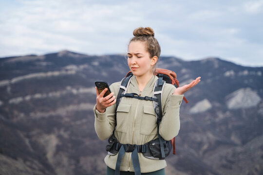 Young female traveler with tourist backpack in the mountains uses phone looking for a connection gps application orientation, lost communication, girl with tourist gears lost while hiking