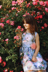 Portrait of little brunette girl in the rose garden sniffs the flowers in summer. Children - Flowers Of Life. The charm of youth