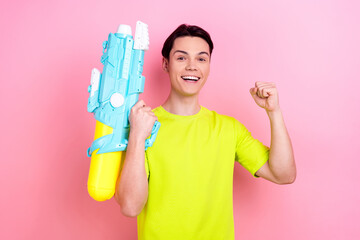 Photo portrait of pretty teenager guy water gun raise fist winning wear trendy yellow outfit...
