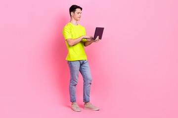 Full length photo of positive dreamy guy wear green t-shirt communicating modern gadget empty space isolated pink color background