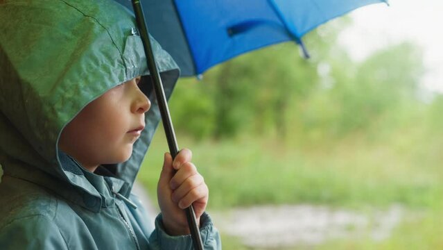 Child in hood hides under umbrella from rain