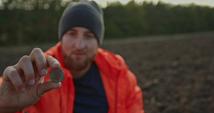 A young man is a treasure hunter. A man holds an ancient coin found with a metal detector.