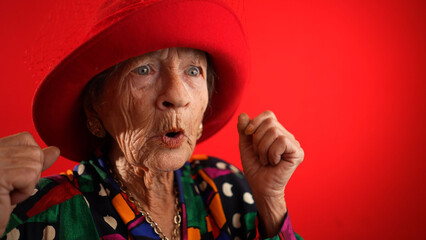 Excited happy fisheye view of funny elderly woman with red hat and no teeth isolated on red...