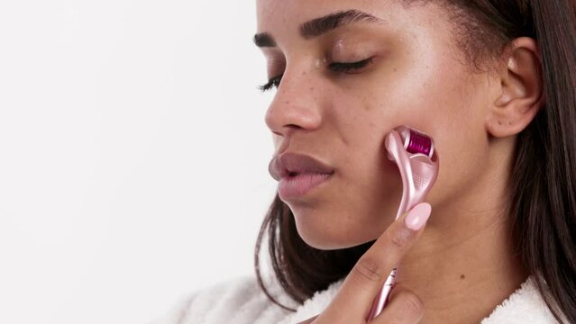 A close-up image of a beautiful young woman using a derma roller on her cheek.