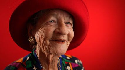 Smiling fisheye view caricature of funny elderly woman smiling with red hat and no teeth isolated on red background.