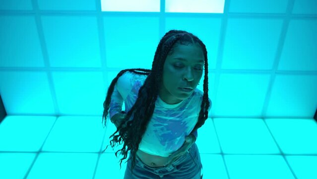 A beautiful Latin girl, African American, dances hip hop music in front of a neon blue background.
Concept of energy, freedom and love for music