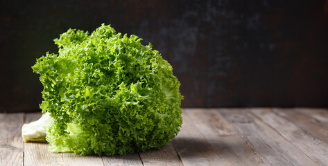 A large bunch of fresh lettuce leaves on a wooden table and a dark background.