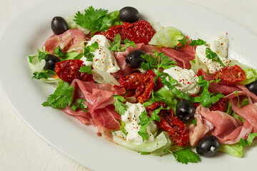 salad with dried tomatoes, prosciutto, soft cheese, olives, homemade, top view,