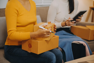 Asian SME business women use laptop computer checking customer order online shipping boxes at home....