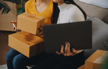 Asian SME business women use laptop computer checking customer order online shipping boxes at home....