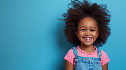 young African American girl with a big smile, wearing a pink shirt and a blue denim jumper, set against a light blue background - Powered by Adobe