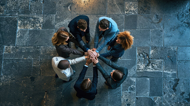 Overhead view of a diverse team of professionals huddled in a circle, placing their hands one on top of the other