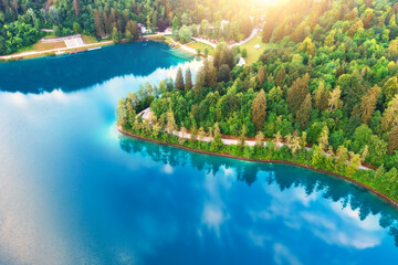 Aerial view of road near blue lake, green forest at sunrise in summer. Bled lake, Slovenia. Travel. Top view of beautiful road, trees in spring. Landscape with highway and sea bay. Road trip. Nature - 758213331