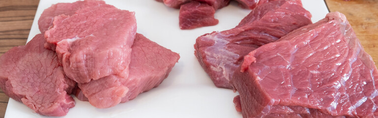 Close up of peases of meat, cutting fresh raw meat on  board in white kitchen. Preparing pork meat,...