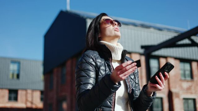Serious woman in eyewear dictating bank card data over phone speaker and getting refusal answer. Disappointed female struggling with lack of money in account and inability of making purchase.