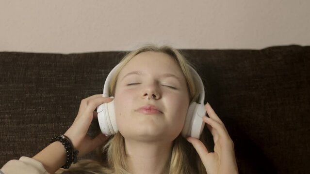 The portrait depicts a Gen Z girl with a nose piercing, lost in the rhythm of the music playing through her headphones. With eyes closed and a smile on her lips, she sings along to the songs,