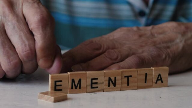 concept of dementia in a pensioner. old man's hands destroy dementia inscription made from wooden blocks. senile diseases.