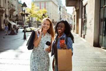 Two happy women with shopping bags and coffee walking in the city
