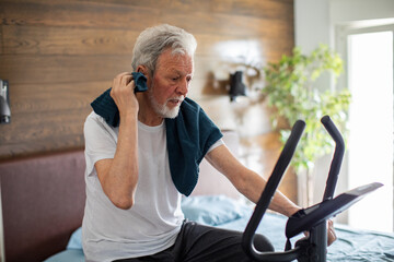 Senior man exercising on a fitness bike in the bedroom at home