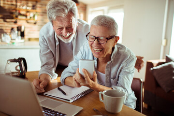 Happy senior couple laughing and looking at smartphone at home