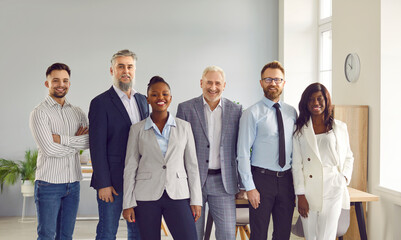 Obraz premium Group of smiling business people posing together in office. Positive successful multiracial business team, corporate office colleagues in formal standing close to each other and looking at camera