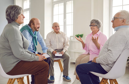 Several old people in group therapy at the retirement home. Senior men and women sitting in a circle, talking about their lives, sharing thoughts and ideas, and taking notes in paper notebooks - Powered by Adobe