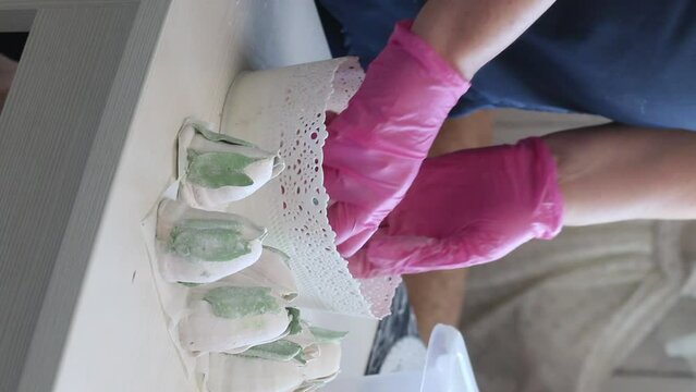 A woman covers a homemade marshmallow with powdered sugar. Tulip buds made of marshmallows with green leaves. Vertical video