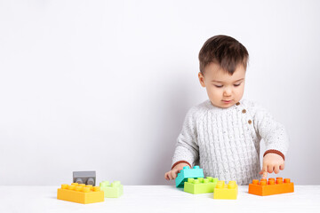 Little cute baby playing with colored blocks constructor, on white background. Educational children's toy.